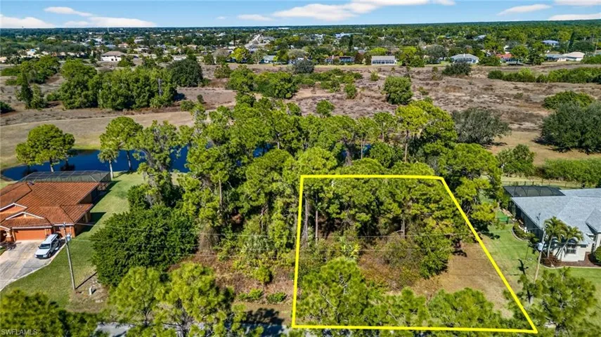 Aerial view of residential area with property parcel outlined and a tree filled landscape