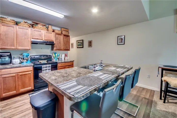 Kitchen with light hardwood / wood-style floors, black range with electric cooktop, sink, an island with sink, and a breakfast bar area