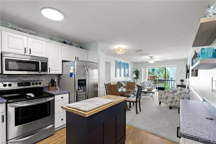 Kitchen with appliances with stainless steel finishes, a kitchen island, wooden counters, open floor plan, and white cabinetry