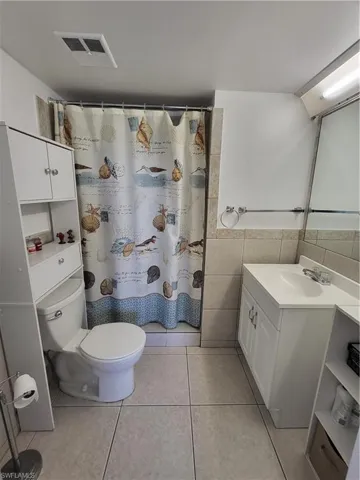 Bathroom 1 with tile flooring, vanity, toilet, and tile walls