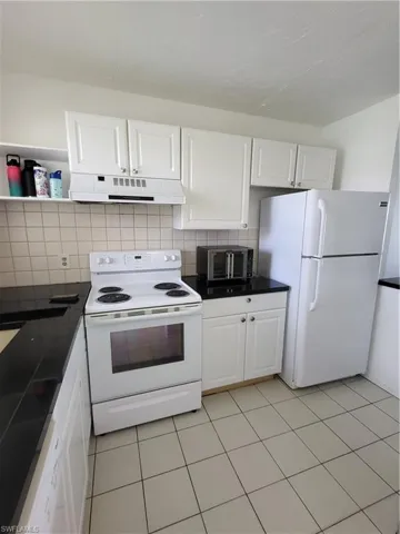 Kitchen with refrigerator, exhaust hood, white cabinetry, and range