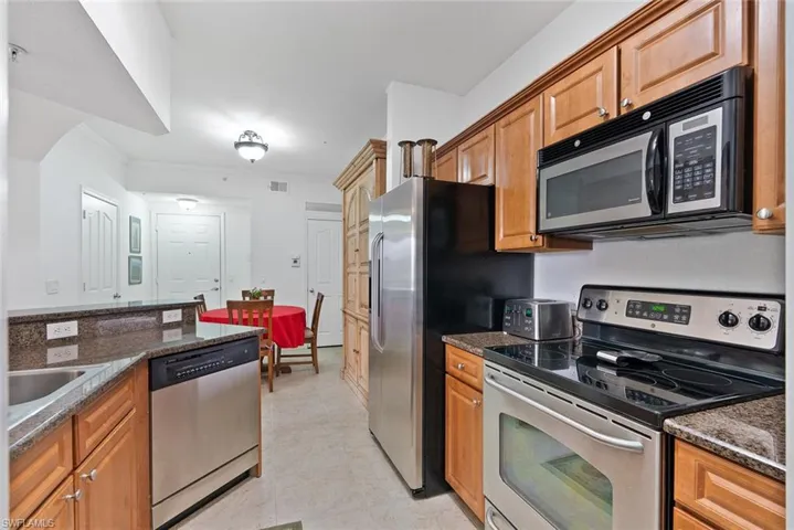 Kitchen featuring stainless steel appliances, dark stone countertops, brown cabinetry, and light tile patterned flooring