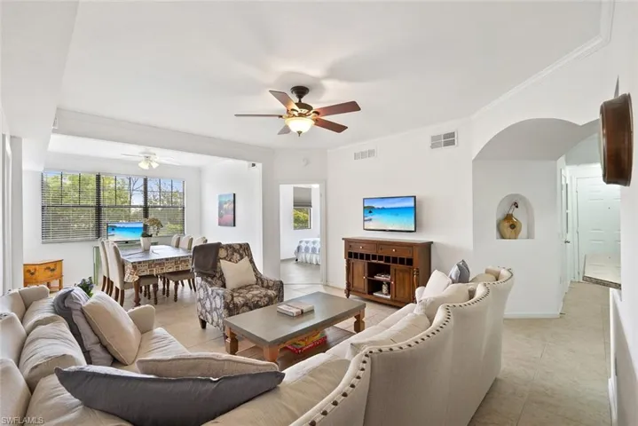 Living room with ornamental molding, light tile patterned flooring, arched walkways, and ceiling fan