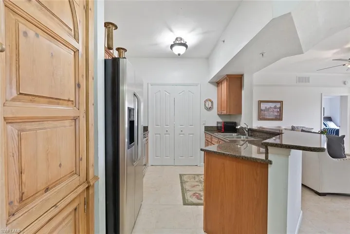 Kitchen featuring a peninsula, dark stone countertops, stainless steel fridge with ice dispenser, brown cabinets, and a ceiling fan