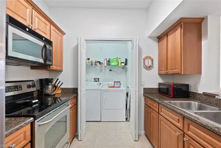 Kitchen with washer and dryer, stainless steel appliances, brown cabinetry, light tile patterned floors, and dark stone counters