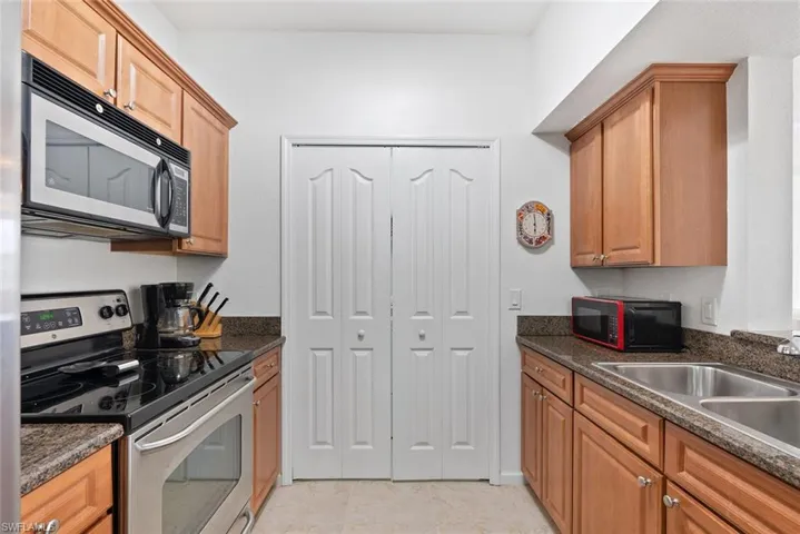 Kitchen with appliances with stainless steel finishes, light tile patterned floors, brown cabinetry, and dark stone counters