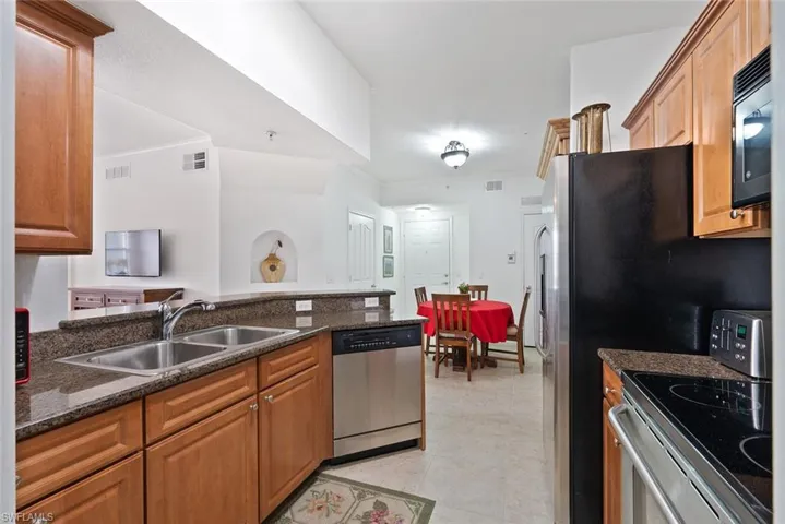 Kitchen featuring appliances with stainless steel finishes, brown cabinetry, dark stone countertops, ornamental molding, and light tile patterned flooring