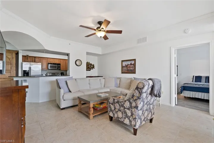 Living area with crown molding, ceiling fan, light tile patterned flooring, and arched walkways