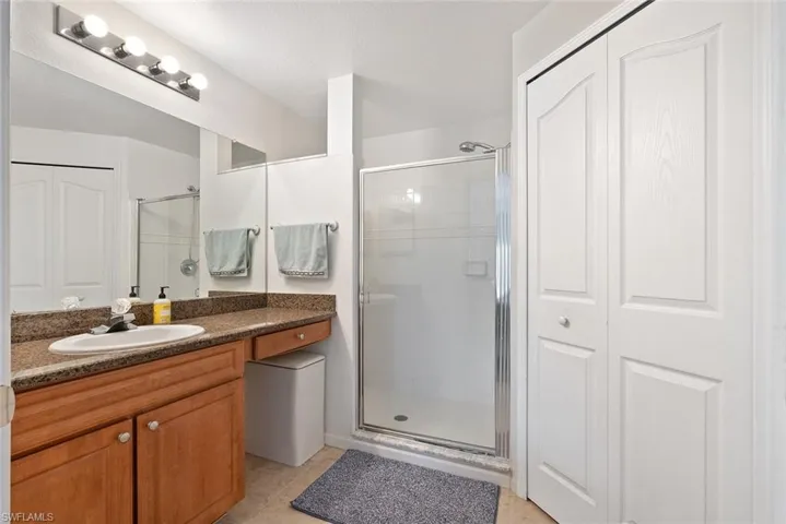 Bathroom featuring a closet, vanity, light tile patterned floors, and a stall shower