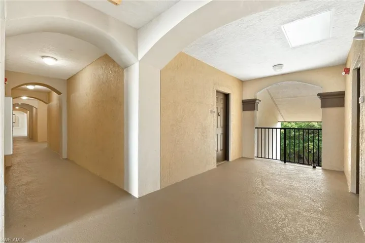 Hallway featuring a textured wall, a textured ceiling, arched walkways, and concrete floors