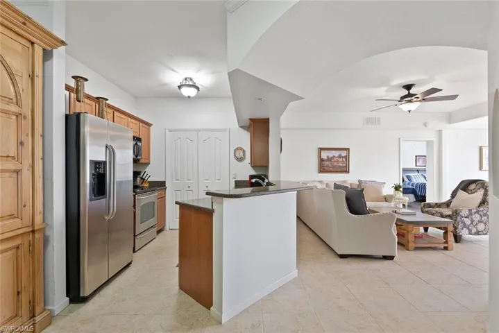 Kitchen with stainless steel appliances, open floor plan, brown cabinets, a ceiling fan, and light tile patterned floors