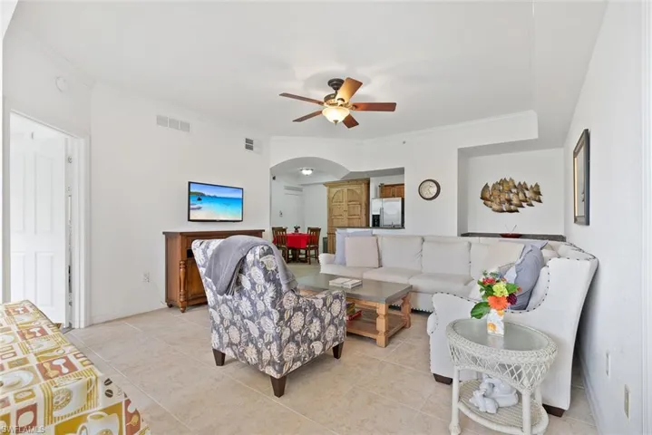 Tiled living room with arched walkways, ornamental molding, and ceiling fan