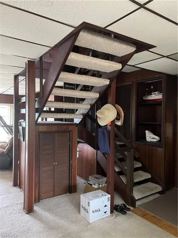 Stairway with carpet flooring, wood walls, and a drop ceiling