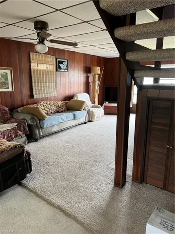 Living room featuring carpet flooring, wood walls, and ceiling fan