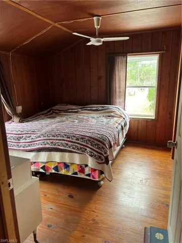 Bedroom featuring wood walls, light wood-style flooring, ceiling fan, and lofted ceiling