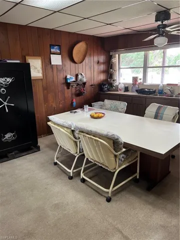 Dining area featuring light carpet, wood walls, ceiling fan, and a drop ceiling
