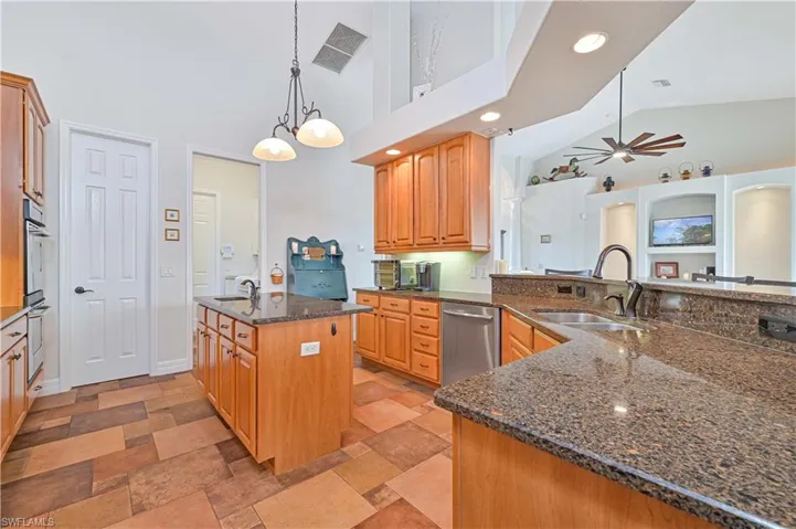 Kitchen featuring hanging light fixtures, sink, appliances with stainless steel finishes, and an island with sink