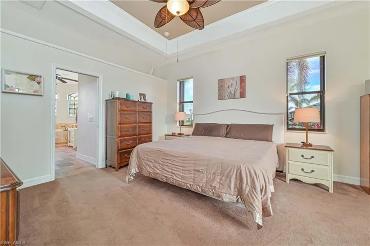 Bedroom with light carpet, ensuite bath, ornamental molding, a raised ceiling, and ceiling fan