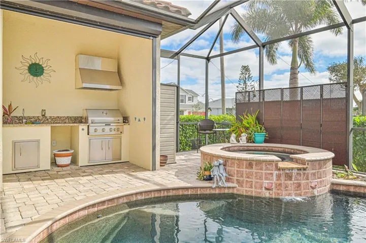 View of swimming pool with glass enclosure, an in ground hot tub, a grill, exterior kitchen, and a patio