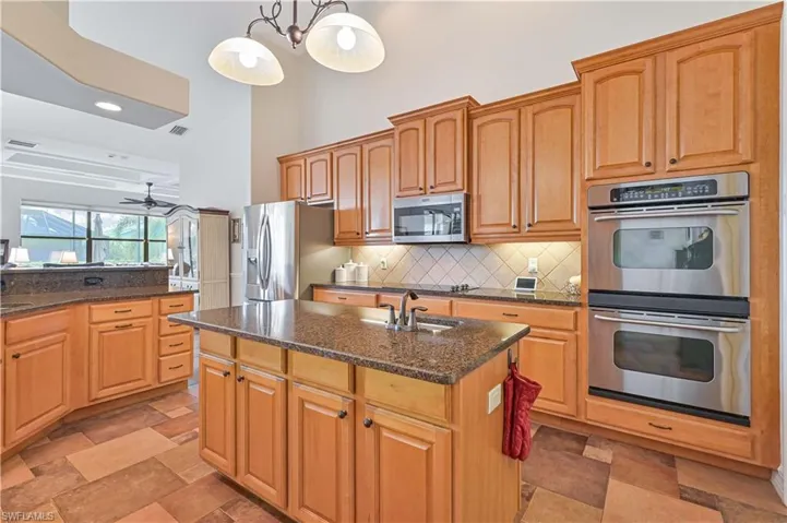 Kitchen with a kitchen island with sink, ceiling fan, appliances with stainless steel finishes, tasteful backsplash, and decorative light fixtures
