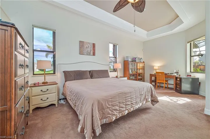 Bedroom with a raised ceiling, multiple windows, ceiling fan, and carpet floors