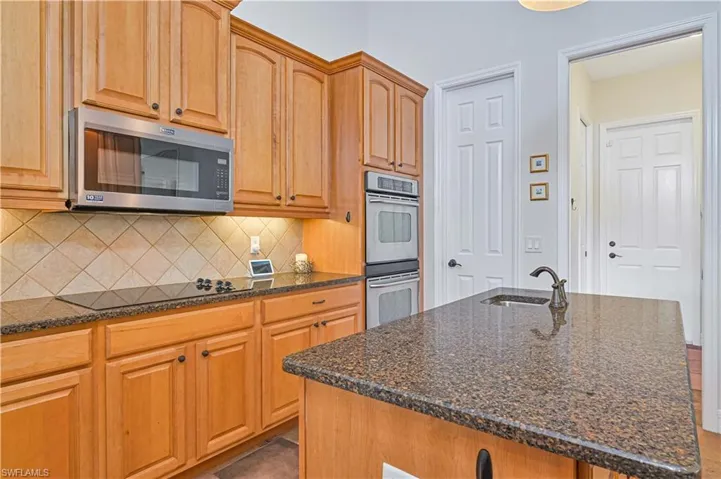 Kitchen featuring backsplash, dark stone counters, stainless steel appliances, a kitchen island with sink, and sink
