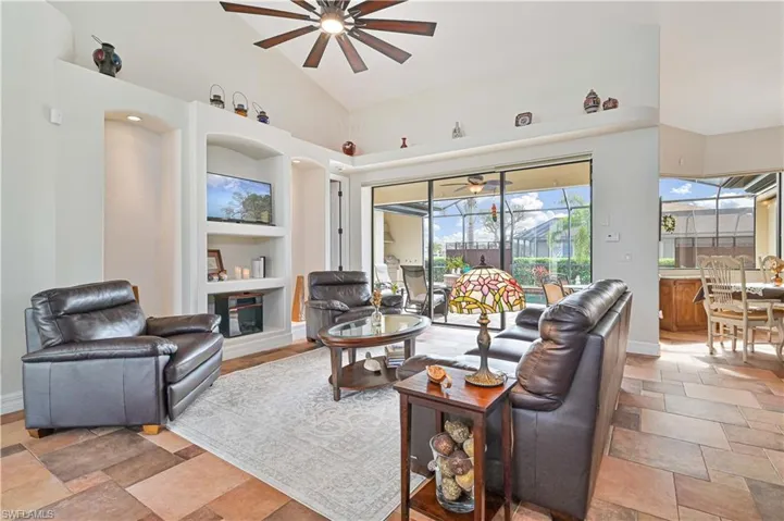 Living room with ceiling fan, built in features, and high vaulted ceiling