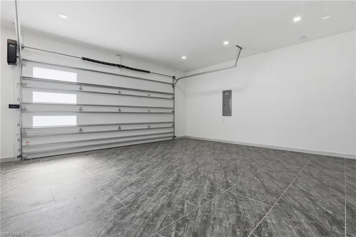 Spacious garage featuring a modern overhead door with translucent panels, automatic opener, recessed ceiling lighting, and contemporary gray tile flooring