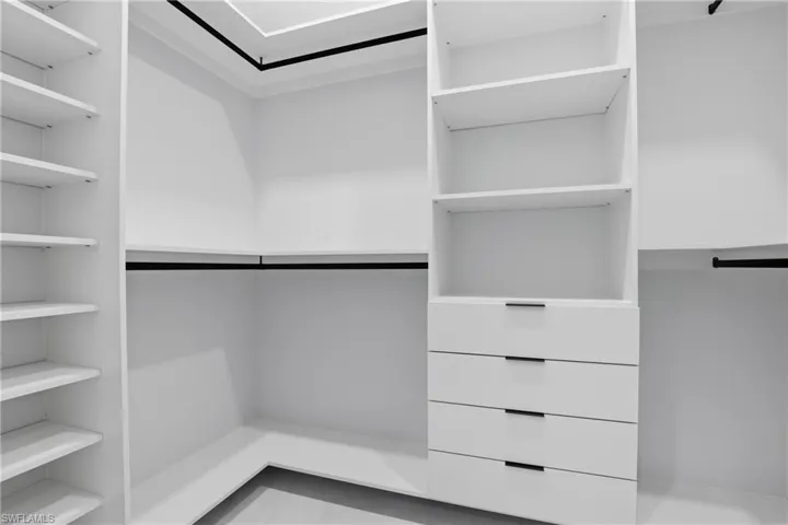 Custom closet system featuring white shelving, multiple hanging rods, and integrated drawers with dark hardware