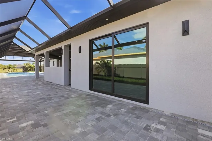 Expansive screened-in patio featuring paver flooring, a sleek sliding glass door, modern exterior sconces, and a built-in outdoor kitchen area