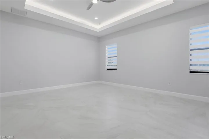Spacious room featuring light gray walls, large format tile flooring, and a tray ceiling with recessed lighting and a ceiling fan
