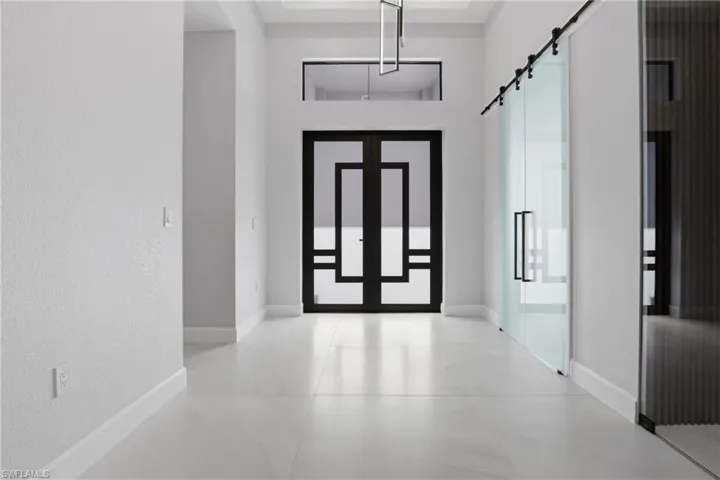 Entryway featuring a large frosted glass barn door, a modern black double-door entry with transom window, high ceilings, and light-toned tile flooring