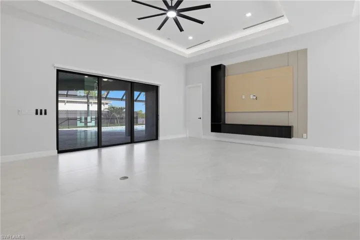 Spacious room with large format tile flooring, tray ceiling with recessed lighting and a modern ceiling fan, and a built-in media console