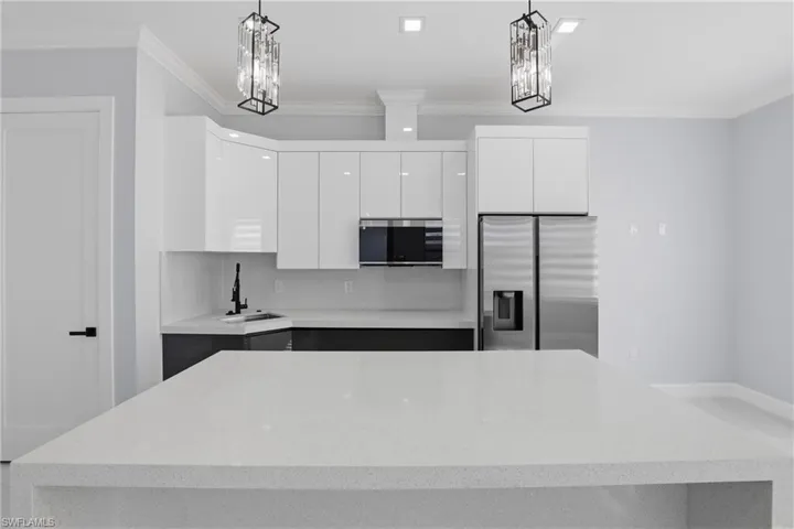 Spacious kitchen featuring a large island with a light-toned countertop, white high-gloss cabinetry, and stainless-steel appliances