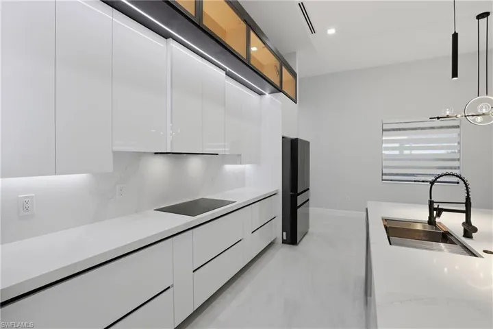 Modern kitchen featuring sleek white cabinetry, integrated cooktop, stone countertops, and a black French door refrigerator