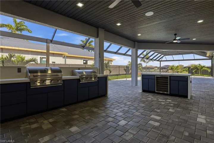Expansive screened lanai featuring an outdoor kitchen with built-in grills, a beverage cooler, and a ceiling fan