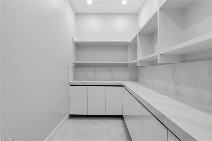 Modern pantry featuring extensive open shelving, crisp white cabinetry, and continuous countertop space with a coordinating backsplash