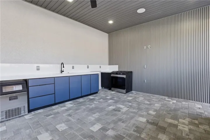 Outdoor kitchen featuring a built-in ice maker, stainless steel range, modern blue cabinetry, white countertops, and a black sink with a gooseneck faucet