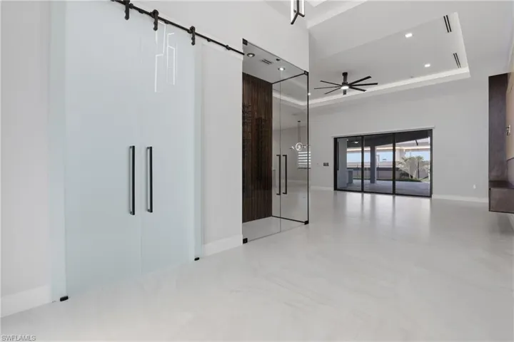 Frosted glass barn doors with black hardware, glass-enclosed entry with dark wood accent wall, recessed lighting, modern ceiling fan, and large sliding glass doors opening to an outdoor patio