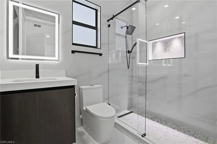 Bathroom featuring a dark wood-finish vanity with an integrated white sink, a backlit mirror, and a walk-in shower with a glass enclosure