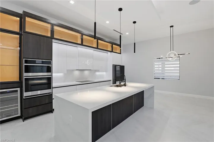 Modern kitchen featuring integrated stainless steel appliances, a built-in wine cooler, a large center island with a sink, white countertop, and dark wood-finish cabinetry