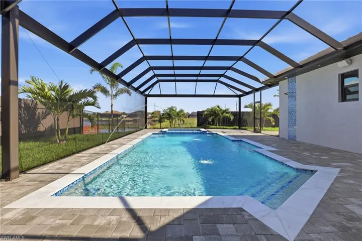 Screened outdoor living area featuring a rectangular pool with integrated spa, paver patio, and decorative pool tile