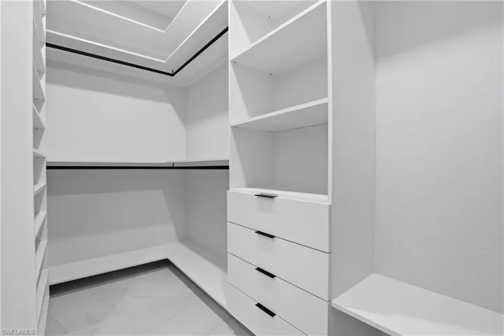 Custom closet system featuring white built-in shelving, hanging rods, and integrated drawers with dark hardware