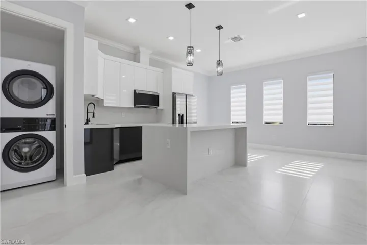 Open-concept kitchen featuring an island with a waterfall countertop, white glossy cabinetry, stainless steel appliances, and pendant lighting