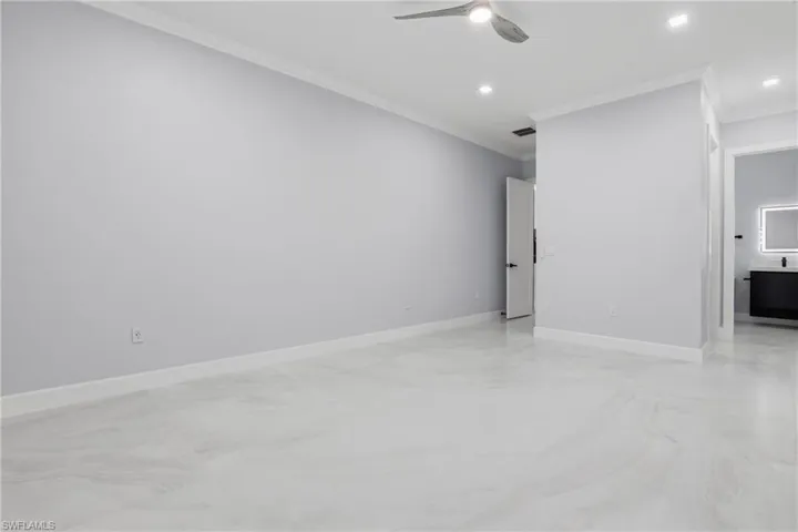 Spacious room featuring light-toned walls, crown molding, and large-format flooring