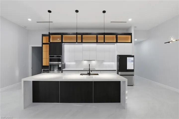 Contemporary kitchen featuring a large waterfall island with integrated sink, sleek dark cabinetry, white perimeter cabinetry, and modern pendant lighting