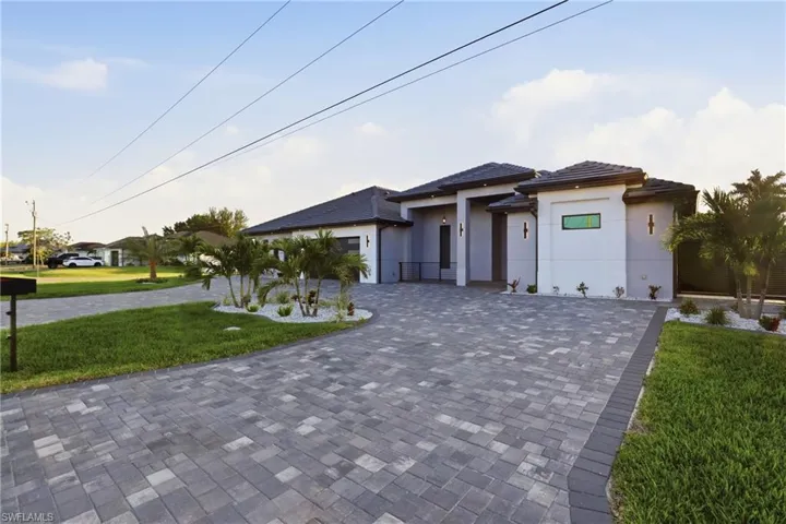 Contemporary home exterior featuring a paver driveway, dark tile roof, and integrated landscaping with palm trees