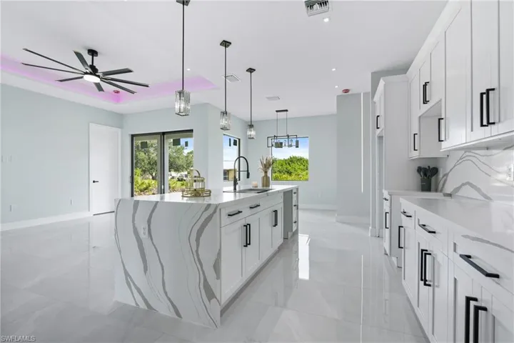 Kitchen with white cabinets, sink, pendant lighting, a kitchen island with sink, and light tile patterned flooring