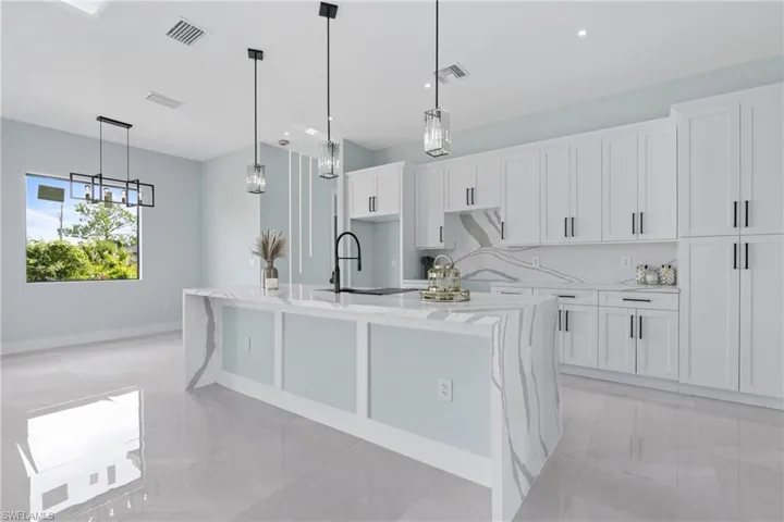 Kitchen featuring light tile patterned flooring, white cabinets, light stone countertops, hanging light fixtures, and a center island with sink