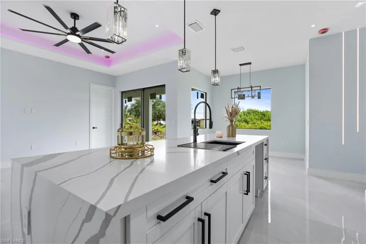 Kitchen featuring white cabinetry, light tile patterned floors, pendant lighting, a raised ceiling, and a center island with sink